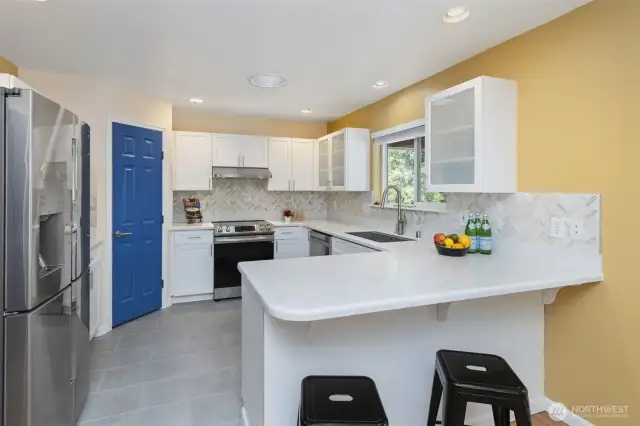 2nd home kitchen with solid surface counter tops, tiled backsplash, new appliances and tile floor.