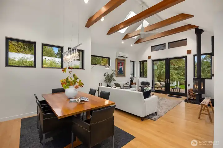 The dining and living room with vaulted ceiling, wood cross-beams, skylights and a ceiling fan.