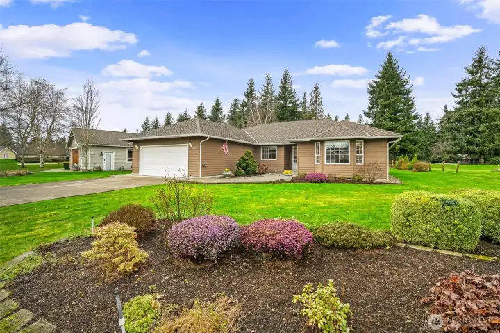 Front yard view showing the expansive lawn, circular planting beds, and mature shrubs framing the home.