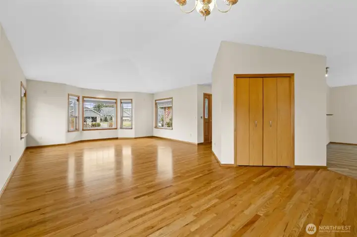 View from the dining area toward the living room showing the hardwood floors, vaulted ceiling, and multiple front facing windows.