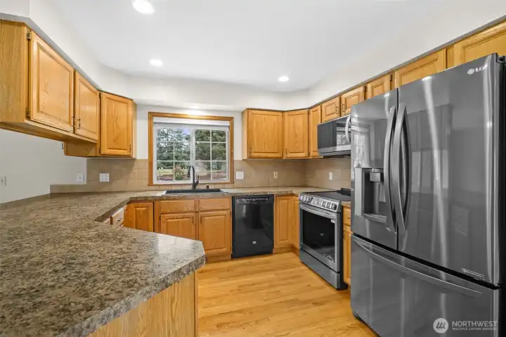 Kitchen with granite countertops, stainless steel appliances, ample cabinetry, and window above the sink overlooking the backyard.