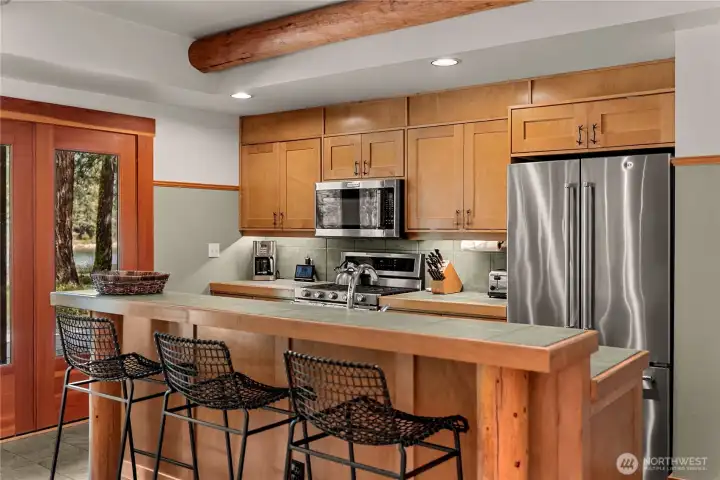 Stainless steel appliances, tile countertops, and maple cabinetry provide a blend of modern style and natural warmth, creating a functional and attractive kitchen space.