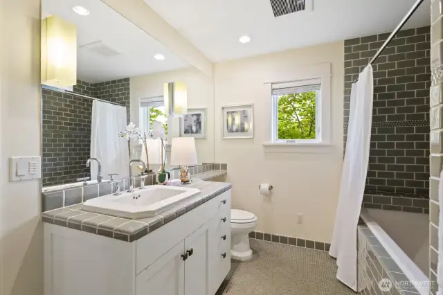 Full bath on the upper level boasts cool green tile details and unique fixtures.