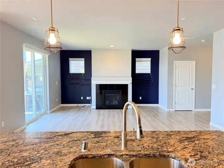 Open-concept kitchen with a view into the spacious living room featuring an electric fireplace and backyard access