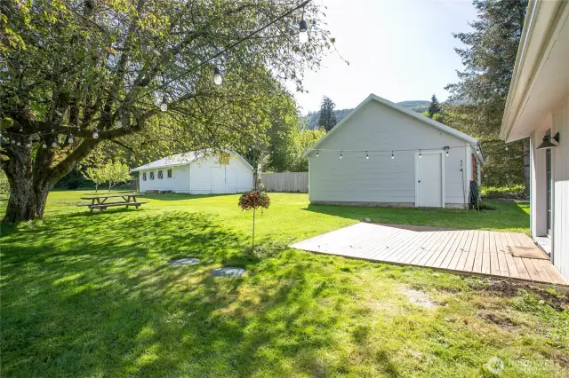 View of the back of the house. Patio area from primary bedroom. View of first outbuilding that has a garage door in the front. View of second outbuilding.