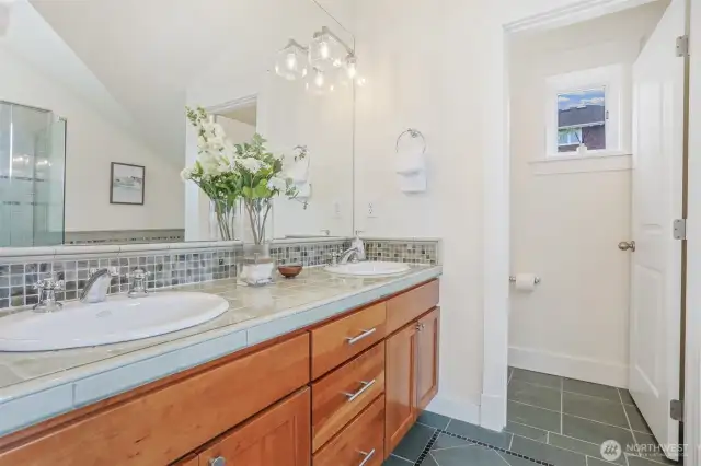 Primary bath has double vanity sink. A mix of ceramic, glass, and slate tile.