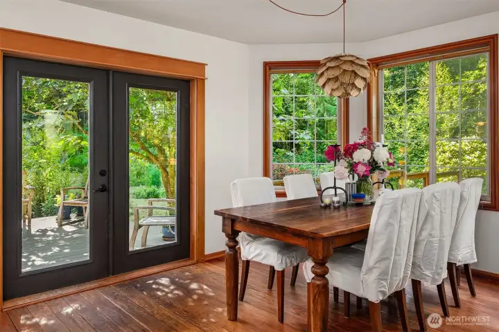 Dining area off kitchen surrounded by windows with french doors out onto deck.