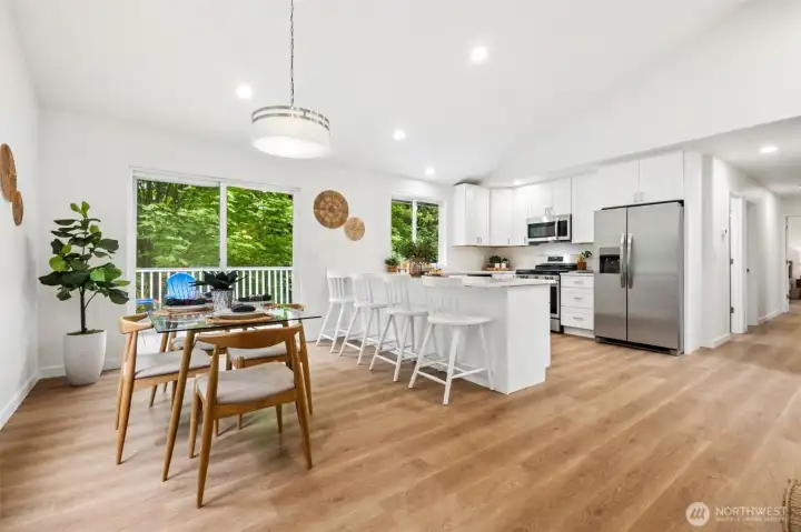 The dining area sits just off the kitchen, offering a comfortable space for meals and conversation. Large windows bring in natural light and frame the greenery outside.