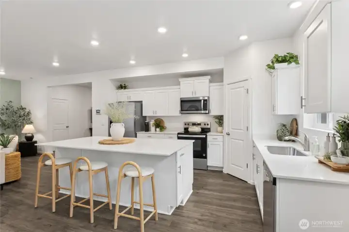 This kitchen view highlights both the large center island with sleek quartz countertop and the perimeter counter with an undermount sink, ample cabinet storage, and stainless steel appliances. Photos are representative only and may display different colors and or upgrades.