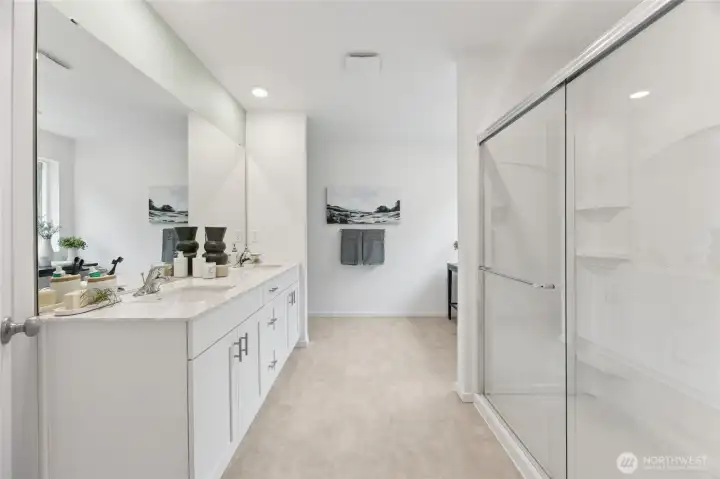The luxurious owner's en-suite bath showcases a wide double-sink vanity, quartz countertops, a large framed mirror and a spacious walk-in shower with glass sliding door. Photos are representative only and may display different colors and or upgrades.