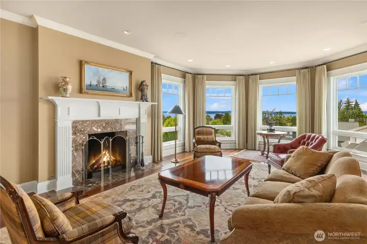The living room with a cove of floor to ceiling windows and a warm wood burning fireplace.