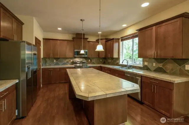 This kitchen sold the current owner!  Large island with tile countertop and tile countertops with tile backsplash and rich wood cabinetry, pendant lighting, newer stainless appliances and large walk-in pantry makes this a delightful place to prepare meals