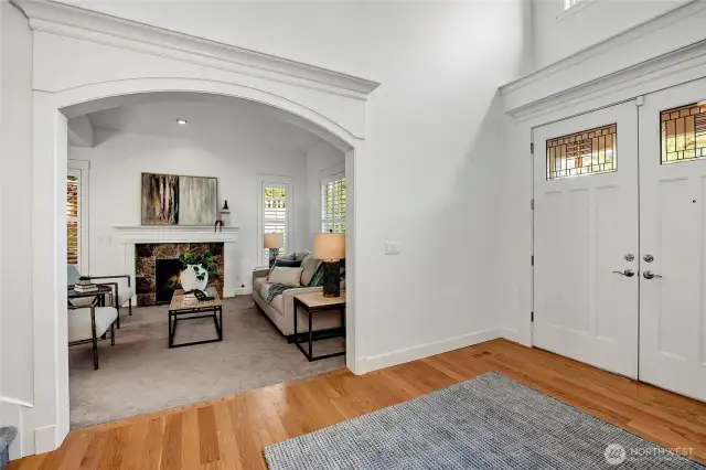 The light-filled entry opens gracefully to the formal living room through a wide arched doorway, showcasing elegant millwork, a cozy fireplace, and a welcoming ambiance perfect for entertaining.