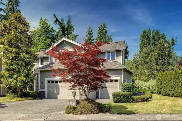 This side of the home features an oversized three-car garage with matching doors, each accented by transom-style windows that enhance curb appeal and allow natural light into the space. A mix of horizontal siding and stonework provides texture and contrast, while a vibrant Japanese maple adds a splash of color to the neatly landscaped front yard. The wide driveway offers generous off-street parking and effortless access to the garage.  This side of the home features an oversized three-car garage with matching doors, each accented by transom-style windows that enhance curb appeal and allow natural light into the space. A mix of horizontal siding and stonework provides texture and contrast, while a vibrant Japanese maple adds a splash of color to the neatly landscaped front yard. The wide driveway offers generous off-street parking and effortless access to the garage.  This side of the home features an oversized three-car garage with matching doors, each accented by transom-style windows