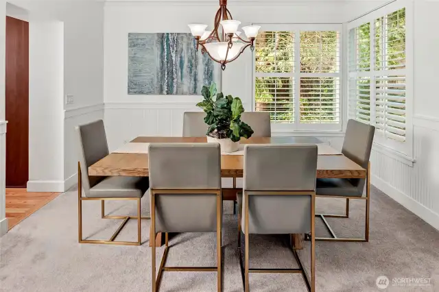 The formal dining room is both elegant and inviting, featuring crisp white wainscoting, a classic chandelier, and oversized windows with plantation shutters that fill the space with natural light.