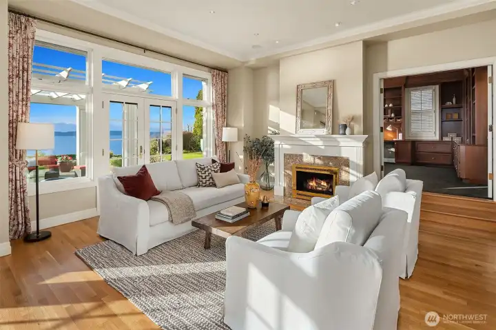 Gas fireplace in the living room with large windows that bring the outside in. Den/library off the Living Room. Kitchen eating area behind you.