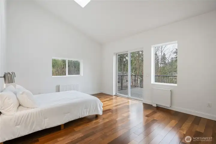 Primary Bedroom with west-facing sliding glass door opening to the deck — perfect for catching sunset views over the lake. Radiator heat, vaulted ceiling, and skylight.