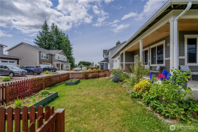 Front yard has beautiful garde  ning, and barely seen on the left are flower beds full of vegetables.