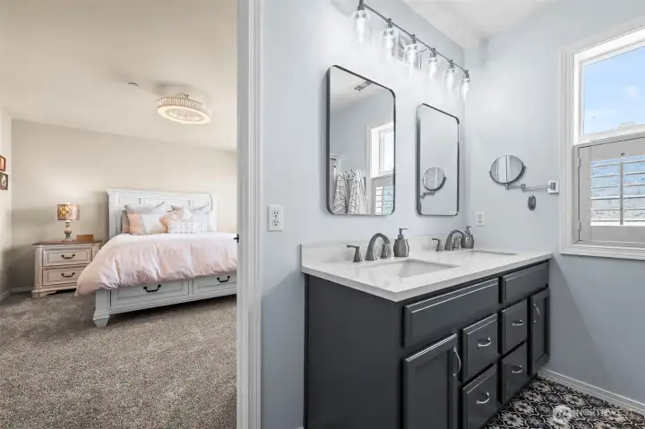 Dual vanities, updated fixtures, and stunning flooring in a primary bathroom with a large shower and linen closet.