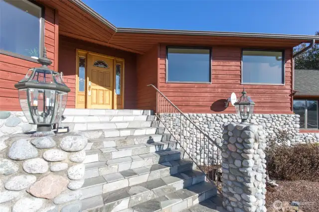 The entryway features a stone slate staircase, and a beautiful custom front door.