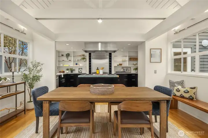 Exposed ceiling trusses painted white, crown the dining room, balanced by windows on each end.