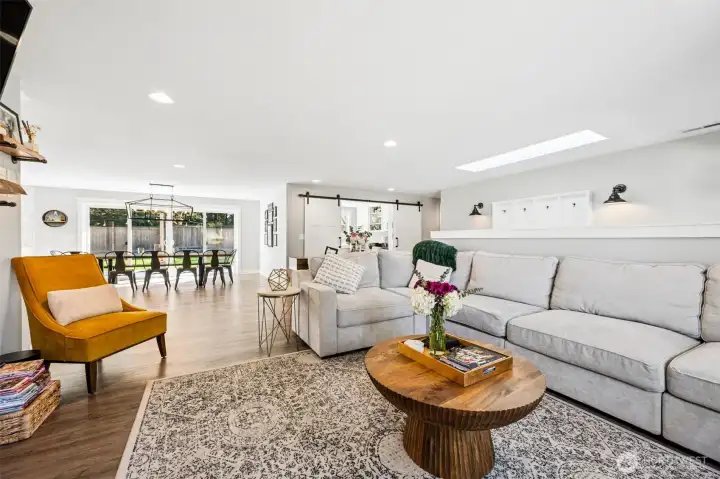 The warm-toned luxury vinyl plank flooring carries your eye straight through the living room into the dining and kitchen spaces, grounding everything with a cohesive, easy-to-live-with feel. The soft neutral palette reflects light beautifully while still adding a bit of depth and personality so it doesn’t feel flat. Off to the side, the barn-style doors to the office or den add a touch of character and flexibility depending on how you use the space. And then there’s that oversized multi-panel double sliding glass door pulling in a ton of natural light and opening the whole back of the home up to the yard.