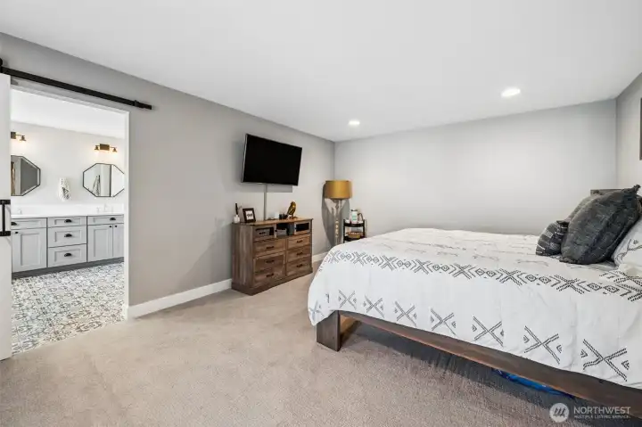 Rest and recharge in this primary suite that keeps things calm, spacious, and easy to live in. The soft dove gray walls and warm latte-toned carpeting create a relaxed, cohesive feel that carries through the home, while the generous size gives you room to truly spread out. There’s already a TV mount in place, so getting set up is simple, and the barn door leading into the ensuite adds a nice touch of character while keeping things functional. Being on the main level is a huge advantage, no stairs to think about, just easy, everyday access that works now and continues to work over time.