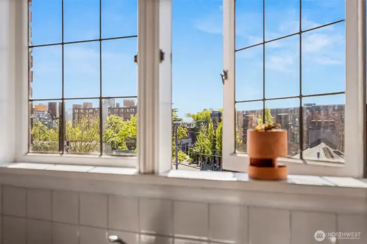 Sunlit kitchen windows frame treetop and city views, adding warmth and character to the everyday routine.