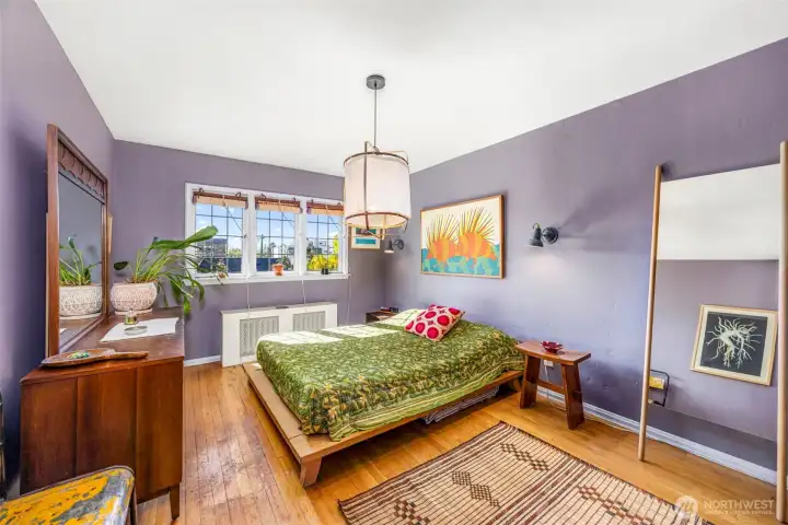 Serene primary bedroom with soft lavender tones, vintage details, and oversized windows overlooking the courtyard greenery.