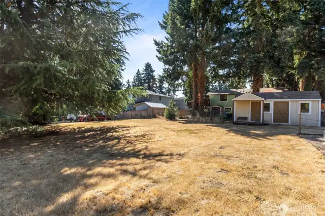 View of fully fenced back yard with playhouse and shed.