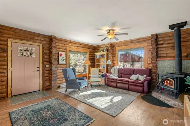 Great Room – Wood Stove View  Gather around the cozy wood stove framed by classic log walls—an inviting focal point that brings warmth, charm, and true cabin character to the heart of the home.