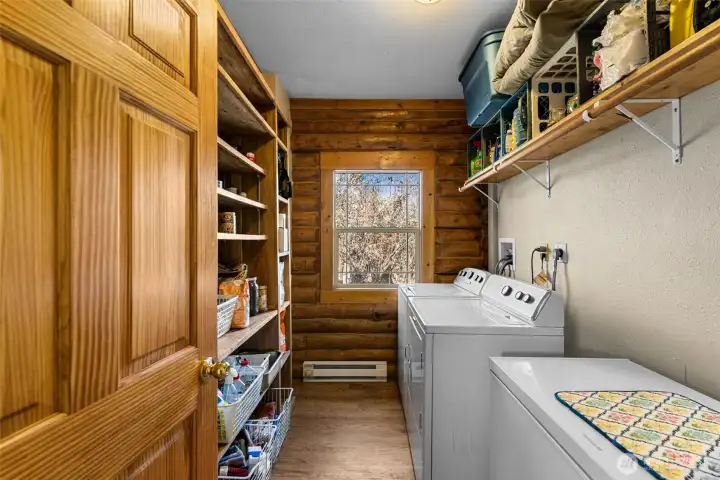 Functional and bright laundry room with washer, dryer, and built-in shelving for organized storage — log accents continue the warm, rustic feel throughout the home.