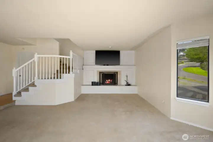 Living area centered around a fireplace with built-in surround and stair access leading to the upper level