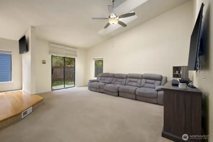Living area with vaulted ceiling, ceiling fan, and sliding door providing access to the backyard