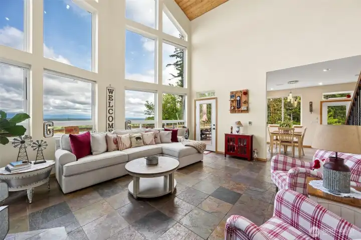 This is one of those layouts that gets the balance exactly right b/c the living room absolutely feels like its own room w/a true focal point, strong architectural definition & enough separation from the dining space to create different moods & gathering zones, yet everything still flows together naturally w/o feeling compartmentalized.  The soaring ceilings, massive windows & heated slate flooring tie the spaces together visually while the partial wall divisions & thoughtful layout keep each area feeling intentional & grounded. Honestly the amount of access this home gives you to the outdoor living spaces is almost comical in the best way possible b/c there are FOUR separate doors b/w the living & dining rooms leading directly onto the 957-square-foot wraparound deck, meaning the Olympic Mt. views are never more than a few steps away no matter where you are standing. This house was very clearly designed around the scenery & understands PNW beauty.