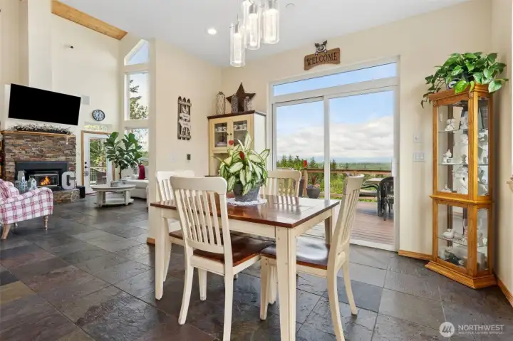 The flow between the dining room and great room is incredibly well balanced here because the spaces feel connected and open without losing their own identity, which honestly is harder to pull off than most builders realize. A thoughtfully placed partial wall creates just enough architectural separation to define the dining area while still allowing natural light, fireplace views and conversation to carry freely throughout the entire main level. From the dining room you can look directly toward the great room, catch the warmth of the fireplace to the side and still stay fully connected to everything happening around you, making the whole layout feel social, relaxed and wonderfully livable. Heated slate floors continue seamlessly throughout the spaces bringing in all that gorgeous earthy movement and texture, while the sliding glass doors opening to the wraparound deck flood the room with natural light and pull the Olympic Mountain setting right into the heart of the home.