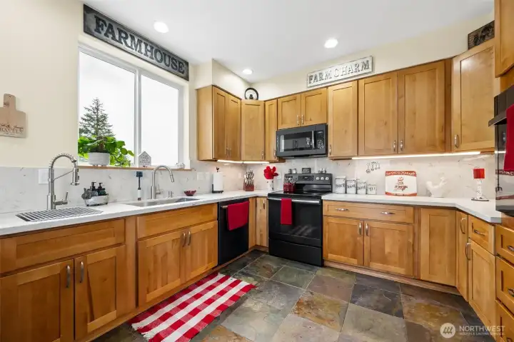There is something deeply satisfying about a kitchen that feels both beautiful AND wildly functional, and this one absolutely pulls that off. Between the dual sink setup, expansive granite counters and multiple cooking zones, the entire space feels designed to support real entertaining instead of just looking pretty in photos. One sink serves as a prep station with a more commercial-style faucet and integrated rack system, while the large undermount sink sits in front of the oversized window where you can soak in mountain views while white granite counters brighten the entire kitchen and provide tons of workspace. Undercabinet lighting adds warmth and depth against the shaker cabinetry and natural slate flooring below and the black appliance suite ties beautifully into the darker slate tones. The electric range setup offers extra ease and peace of mind during busy cooking sessions without worrying about open gas burners getting bumped mid-chaos, plus the additional built-in wall oven m