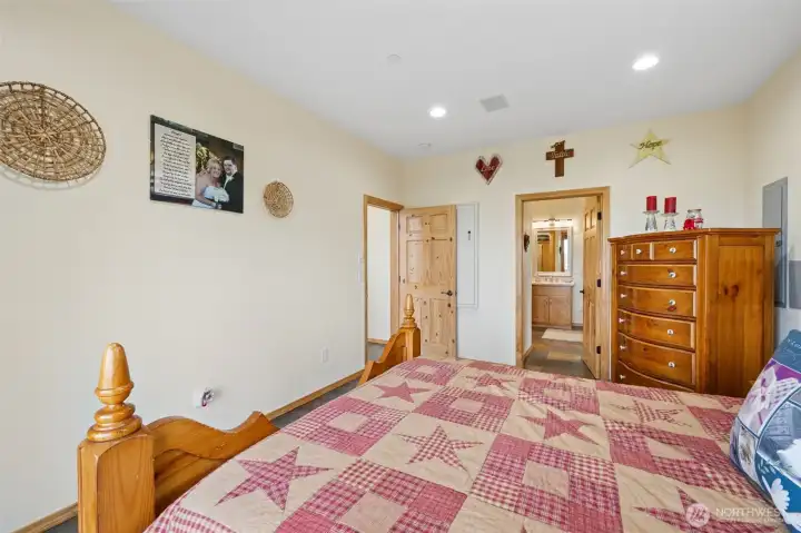 Here is the practical side of the primary suite while still keeping all the warmth and character intact. The room feels spacious and grounded with the continued slate flooring, warm tones and pine six-panel doors carrying the mountain-home aesthetic throughout, while thoughtful details add a little extra functionality behind the scenes. One door conceals a substantial wall safe for valuables and important items, which feels extremely on-brand for a property that also includes a reinforced foundation pinned into bedrock and multiple welded safes in the shop because this home clearly likes being prepared for absolutely everything. The gray wall section behind the dresser provides access to another safe and could easily be disguised with artwork depending on furniture placement if desired. Another door leads directly into the en suite bathroom, creating a comfortable private retreat setup that feels tucked away and separate from the rest of the home.