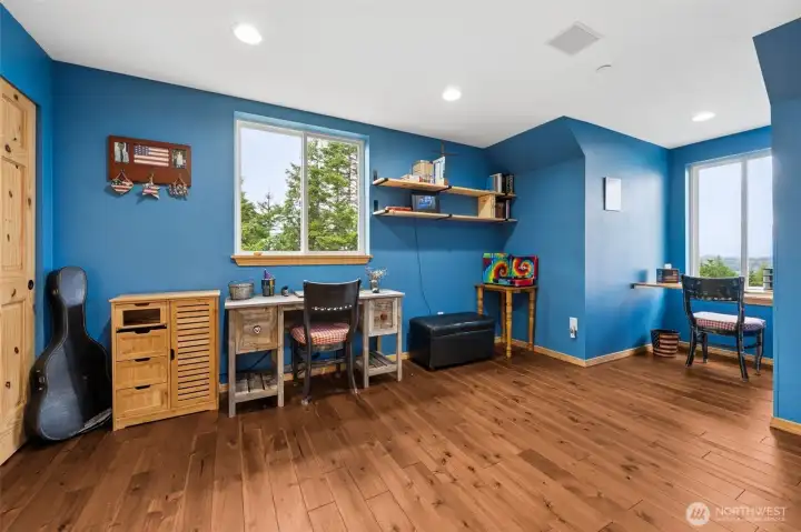 This upstairs bedroom at roughly 12 x 20 feet, is incredibly generous and absolutely drenched in natural light, while the jaw-dropping views looking out across the backyard deck toward the Olympic Mountains and even glimpses of Mount Rainier from the other bedroom are amazing! Gorgeous hardwood floors continue throughout the upstairs level adding warmth and richness beneath the vaulted ceilings, while the handsome blue wall color gives the room a calm grounded feel that works beautifully with the natural wood details and surrounding scenery. A second window captures additional territorial views from another direction, the deep closet offers excellent storage behind a pine six-panel door and recessed lighting plus built-in ceiling speakers continue the thoughtful whole-home audio setup carried throughout the property. Expanded broadband infrastructure is also expected to continue improving throughout the area moving forward.