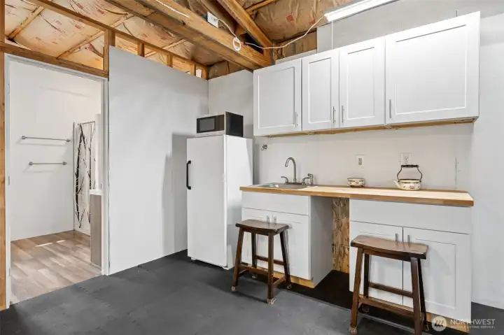 This closer look at the unfinished apartment above the shop really highlights how much infrastructure is already in place for future finishing because this is far beyond just “empty bonus space.” The kitchenette area already includes white shaker cabinetry along with the included refrigerator and microwave, while the attached three-quarter bathroom provides a shower, sink and toilet setup that immediately increases the flexibility and usability of the entire upper level. Tucked neatly into the kitchenette area is a dedicated water heater serving the apartment bath, helping keep the systems separated and functional for future guest or extended-use scenarios. And below, inside the massive shop structure itself, you will also find TWO 3,000-gallon cistern holding tanks supplied from the well lower on the property, with the separate pump house operating on its own power service. This property genuinely feels engineered for long-term functionality and self-sufficiency in a way very few do.