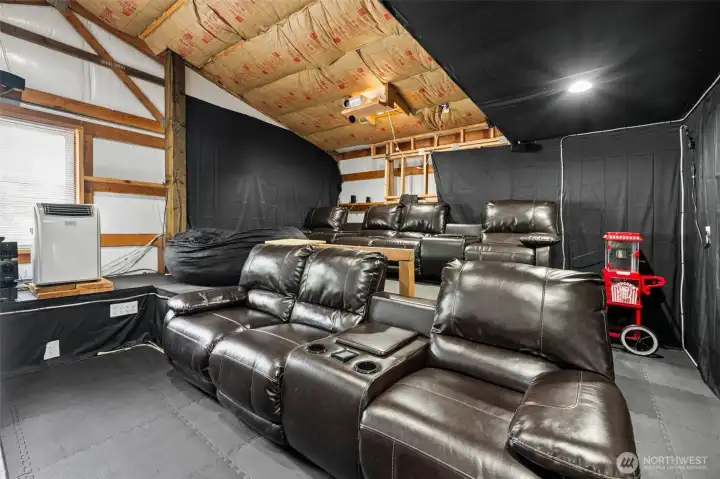 Even unfinished, this vaulted bonus room above the shop already has an incredibly fun and functional vibe thanks to the current theater setup complete with SEVEN reclining movie seats, projector and large viewing screen that transform the space into a private entertainment retreat tucked away above the massive shop below. The vaulted ceilings keep the room feeling spacious rather than tucked away, and behind the portable air conditioning unit there is also a window with blinds bringing in natural light and beautiful surrounding territorial views. The portable A/C unit remains with the property and the layout still leaves room for future customization depending on how the next owner wants to evolve the space over time. There is even additional room nearby for a potential future second bathroom addition if desired, making this unfinished bonus area feel loaded w/long-term flexibility whether someone envisions a theater, gaming lounge, office retreat, guest overflow or something different