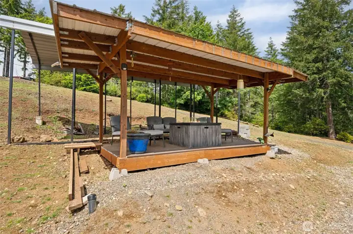 This property keeps proving over and over that it was designed by somebody who truly understood how people actually live, work and play on acreage properties because even the RV setup here is impressively well thought out. Located beside the massive shop is a covered RV carport complete with hookups and water already run directly to the parking area, making it incredibly functional for guests, extended travel setups or full-time RV storage without feeling like an afterthought shoved into a random corner of the property. Right beside the RV space sits a gazebo-style covered deck area creating a surprisingly inviting outdoor hangout zone where you can relax, grill, gather or simply enjoy the peaceful mountain surroundings while staying sheltered from the weather. There is also an RV dump connection conveniently located at the capped pipe beside the deck, while the septic system access lids are tucked discreetly beneath the deck area itself.