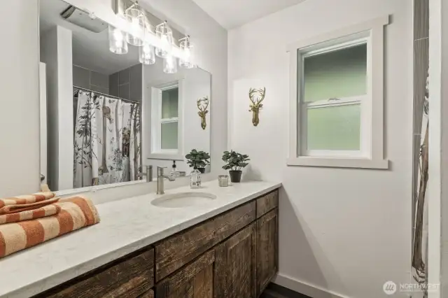 Remodeled main floor 3/4 bath featuring a custom barnwood vanity, quartz countertops, and elegant tiled shower and flooring.