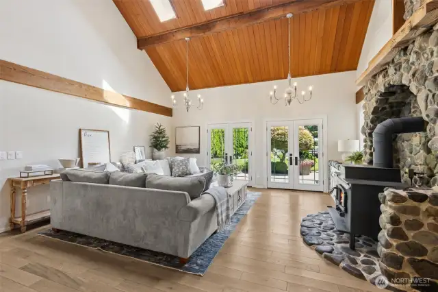 Inviting great room features double French doors to the patio & a striking river rock fireplace w/ wood-burning stove—soaring from floor to vaulted ceiling, it's the heart of the home with warmth & character