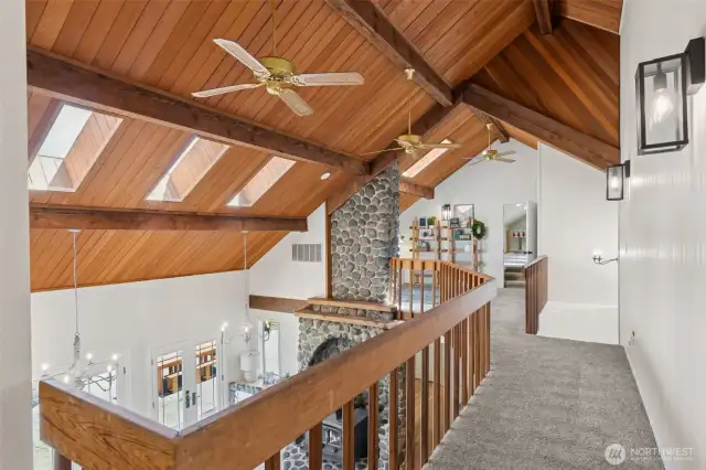 Catwalk view showcases the stunning vaulted ceiling with rich wood detail & skylights that pour in natural light—perfectly framing the grandeur of the 2-story river rock fireplace below