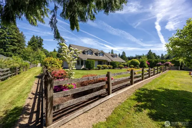 Split rail fence borders the front yard, gracefully defining the garden area—adding charm, structure & a classic touch to the beautifully landscaped entry