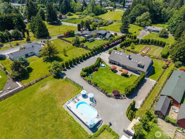 Elevated angle captures both front & back of the property—highlighting the pool, landscaped yard, curved driveway & gravel areas that offer ample parking & space for guests to feel right at home