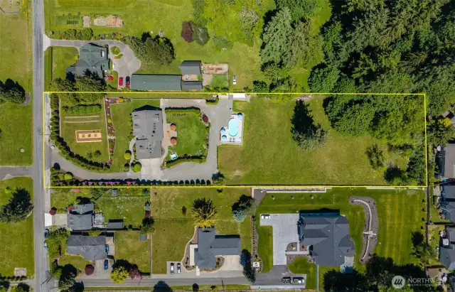 Overhead aerial view outlines the full scope of the property—curved driveway entry, manicured gardens, expansive home, pool & hot tub, landscaped yard & extended green space leading into a private wooded area