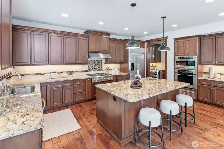 Open Chef's kitchen with slab granite countertops, abundant cabinetry, with soft-close drawers, full-height backsplash, stainless steel appliances, and undermount lighting.