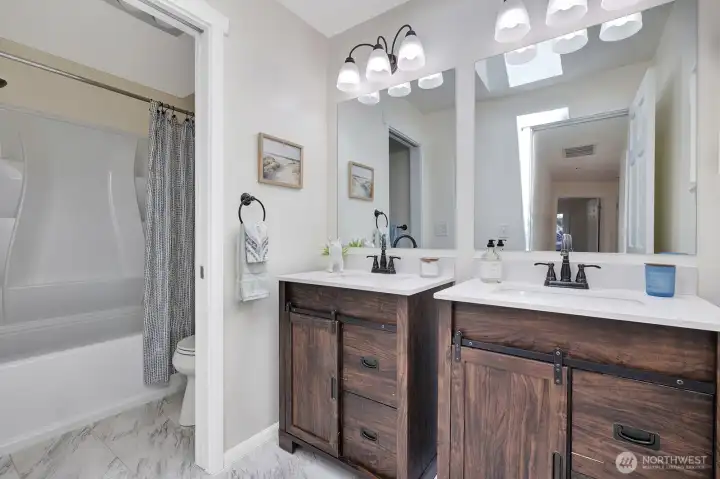 Full, hall bathroom with double vanities has a skylight